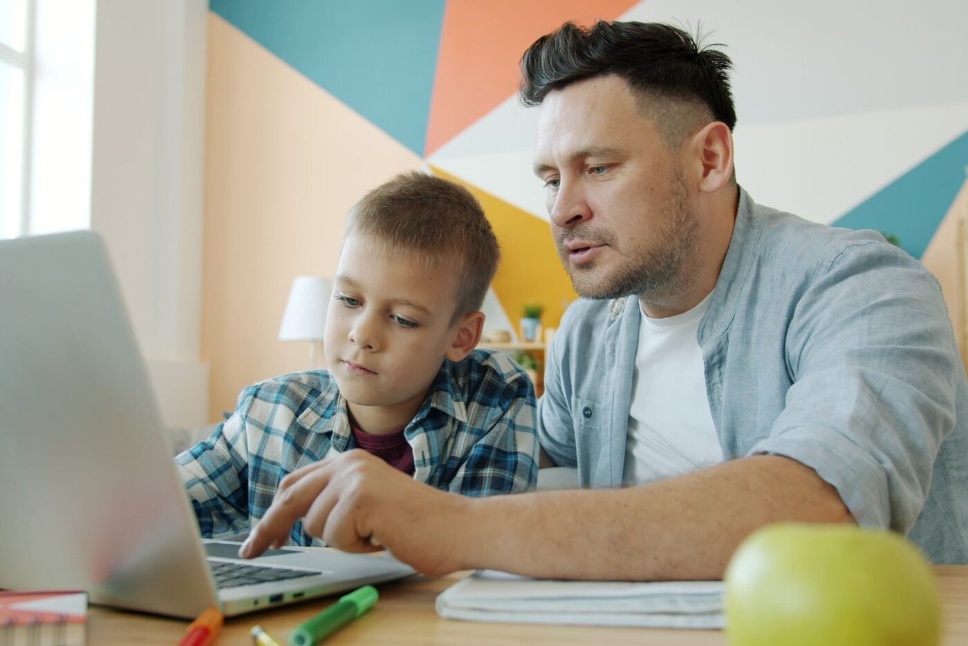 A father and son look at a lesson together on a laptop at home