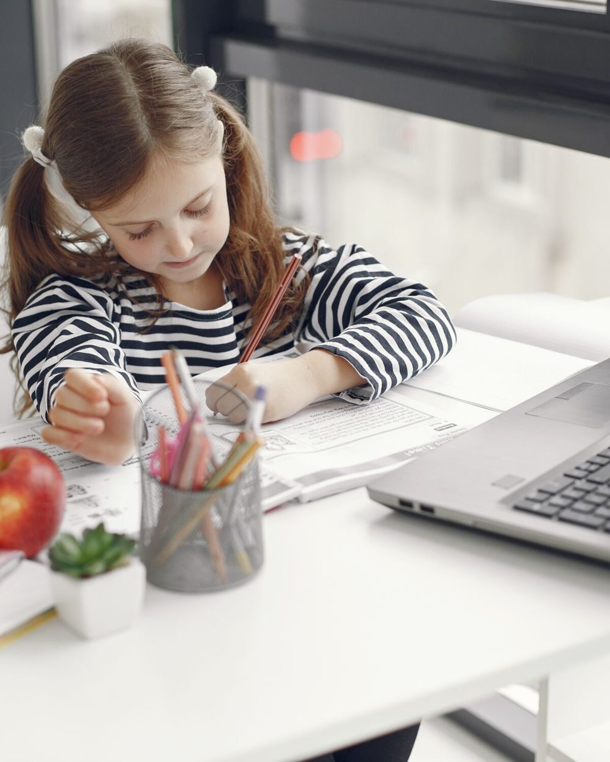 A girl works through a lesson on a laptop at the kitchen table at home